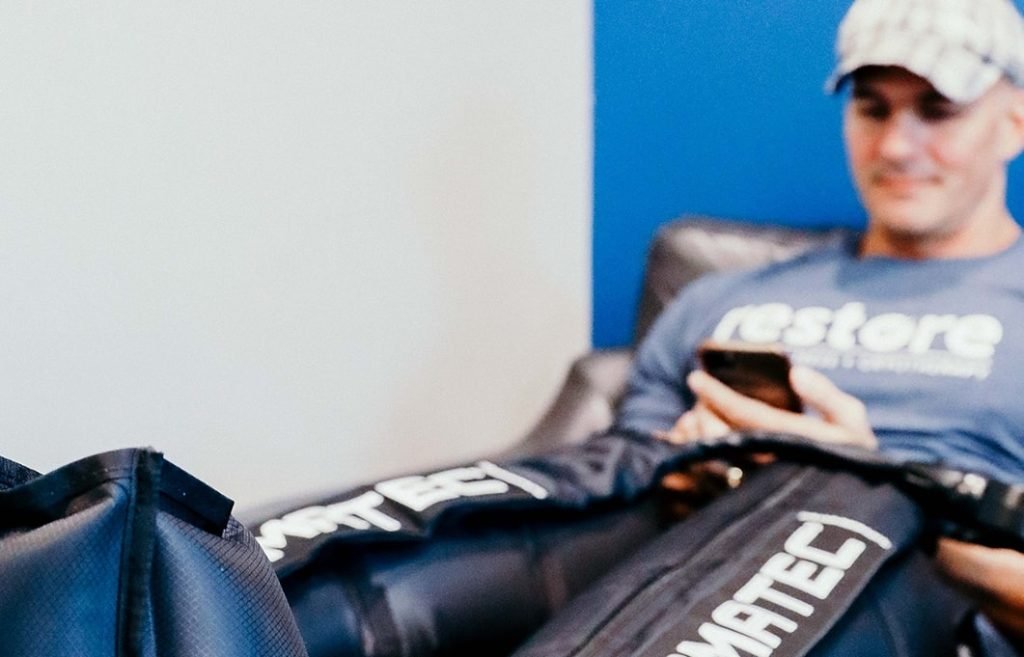 Man looking at his phone while enjoying Compression therapy at Restore Hyper Wellness