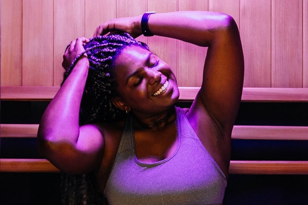 Woman smiling with hands on her head while sitting in Infrared Sauna at Restore Wellness