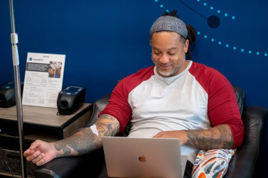 Man with tattoos and red white shirt getting an IV drip.