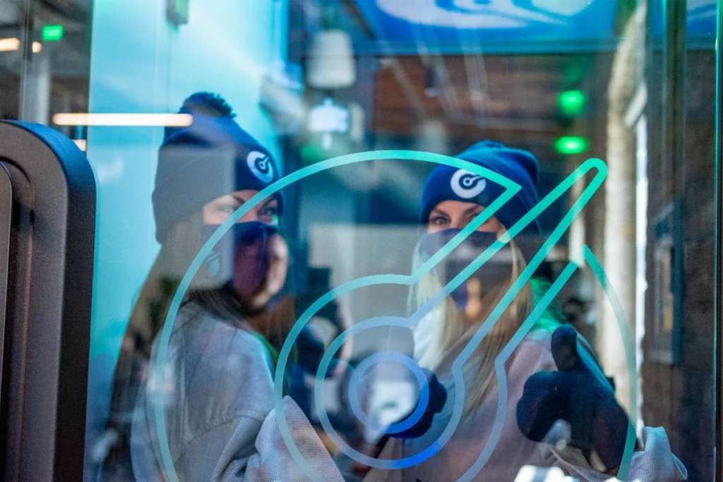 Two women in a cryochamber with beanies smiling. They are giving thumbs up.